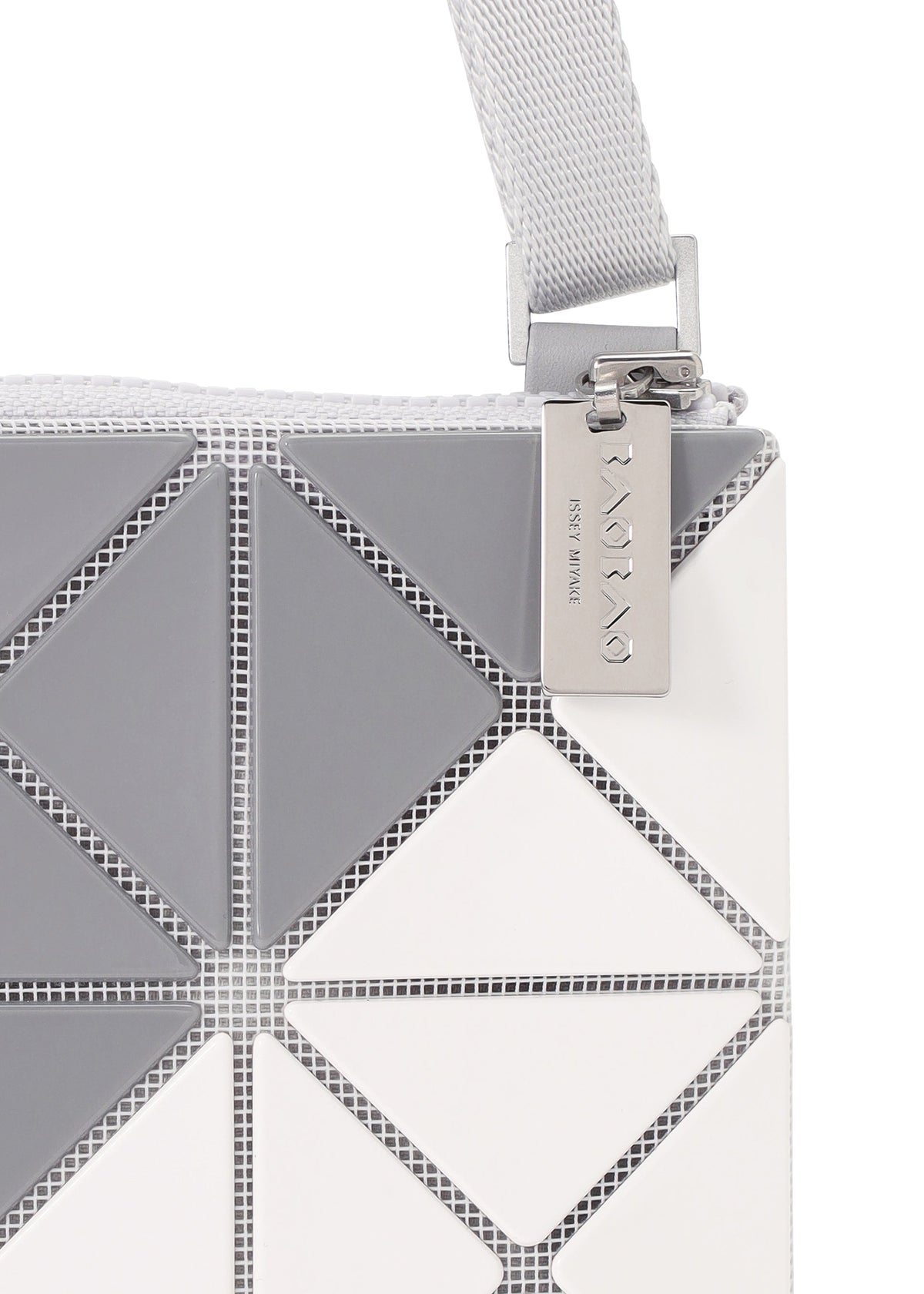 Close-up of the SIGN shoulder bag by BAO BAO ISSEY MIYAKE, featuring a textured gray and white geometric triangular pattern, silver zipper, metallic engraved tag, and light gray woven strap. view 4 of 6