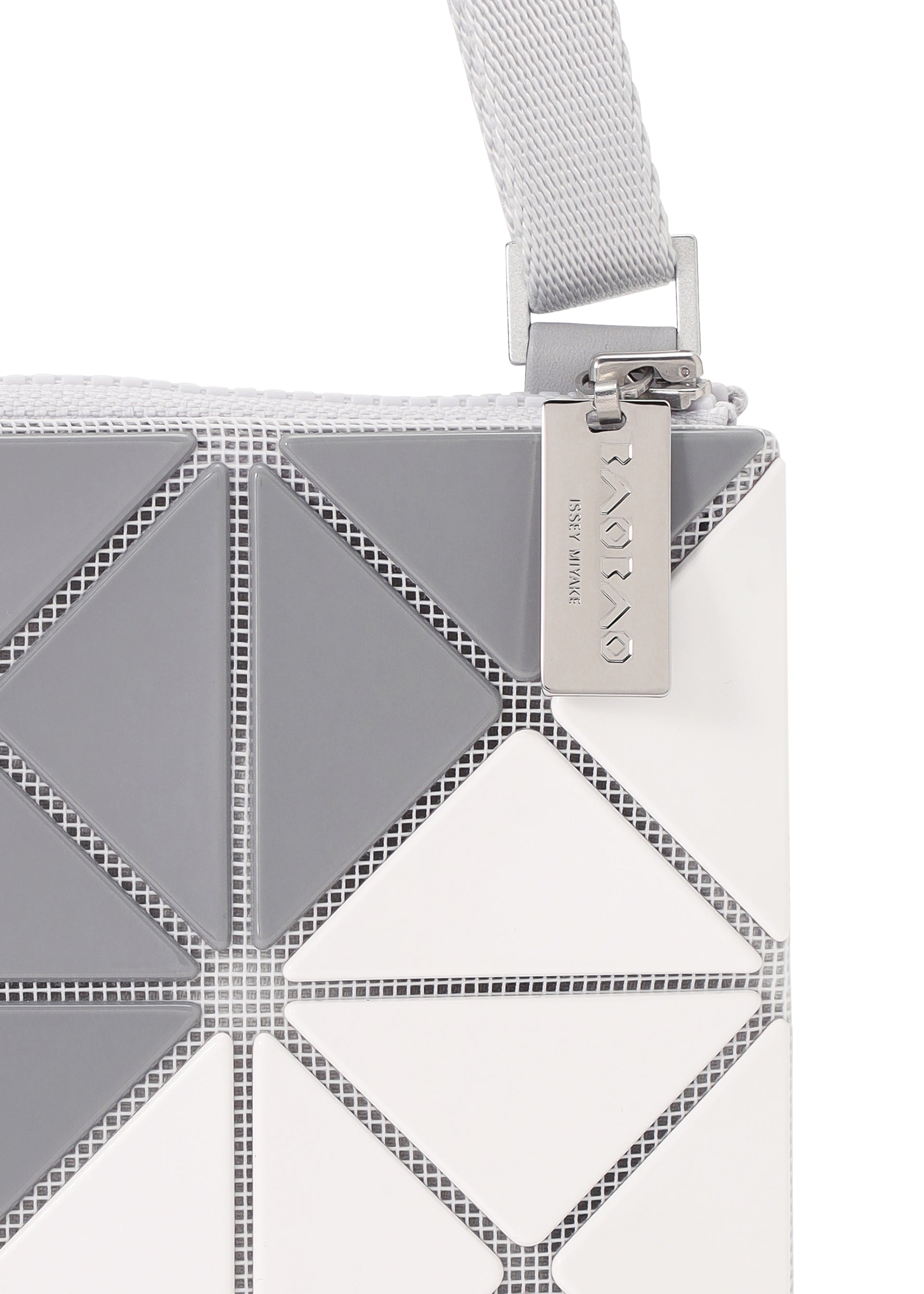 Zoomed view Close-up of the SIGN shoulder bag by BAO BAO ISSEY MIYAKE, featuring a textured gray and white geometric triangular pattern, silver zipper, metallic engraved tag, and light gray woven strap.