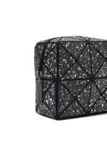 The CITY toiletry bag by BAO BAO ISSEY MIYAKE features black geometric panels with a speckled white and gray pattern, triangular stitching, a zip closure with metal tag, and a sturdy gusset—shown angled on a white background.