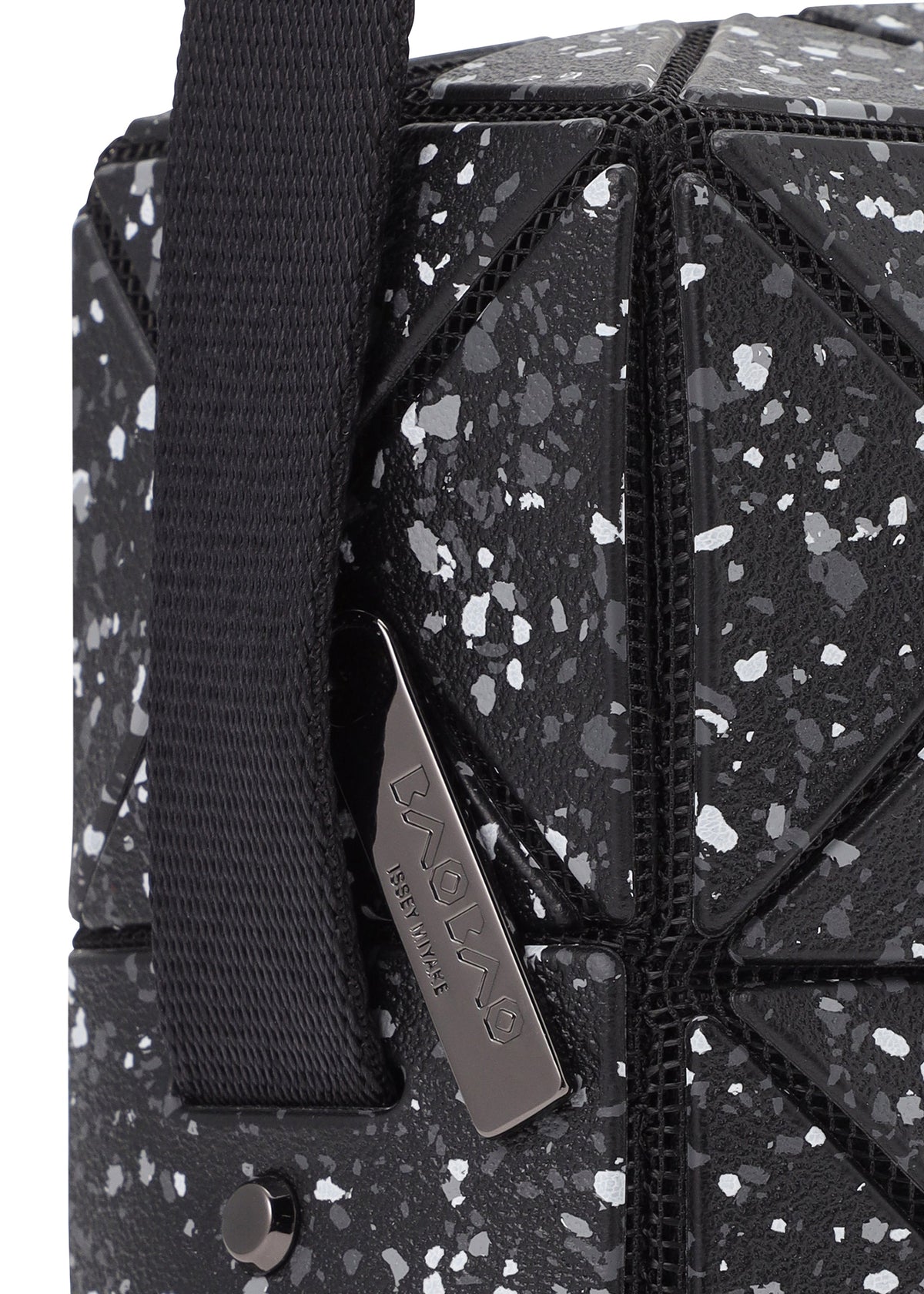 Close-up of the CITY shoulder bag by BAO BAO ISSEY MIYAKE, featuring a black geometric pattern with white speckles, matte leather-like finish, adjustable strap, and a metal tag engraved with the brand name. view 6 of 9