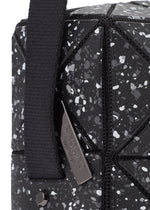 Close-up of the CITY shoulder bag by BAO BAO ISSEY MIYAKE, featuring a black geometric pattern with white speckles, matte leather-like finish, adjustable strap, and a metal tag engraved with the brand name.