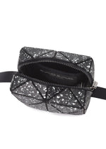 The CITY by BAO BAO ISSEY MIYAKE is a small black geometric shoulder bag with white speckles, a leather-like matte finish, open zipper, black adjustable side straps, and a simple black-lined interior.
