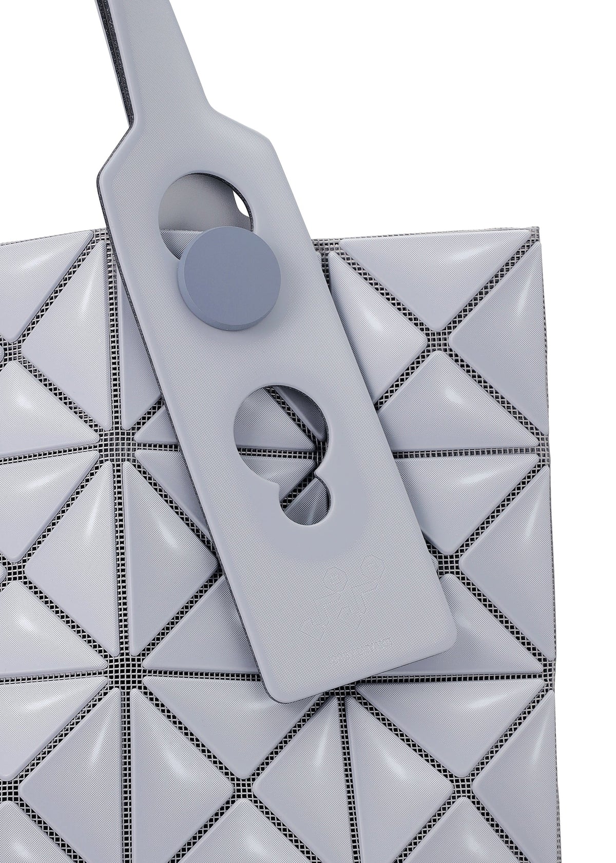 Close-up of the MINIATURE tote by BAO BAO ISSEY MIYAKE, featuring light gray triangular panels, an adjustable handle with circular cut-outs, oversized metal hardware, and a round button on matte leather-like material. view 5 of 9