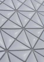 Close-up of the MINIATURE by BAO BAO ISSEY MIYAKE, featuring a geometric grid of raised, glossy white triangular tiles with thin dark lines, evoking modern tote bag hardware.