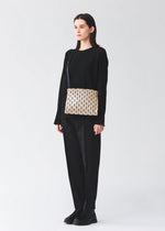 A person stands against a plain background wearing a black outfit and sneakers, carrying the BAO BAO ISSEY MIYAKE ROW METALLIC crossbody shoulder bag with a geometric pattern from the PRISM series.