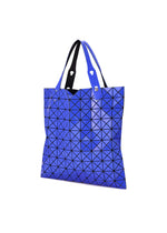A blue PRISM GLOSS tote bag by BAO BAO ISSEY MIYAKE, featuring black triangular patterns and crafted from an enamel-like material with a modern, glossy finish. Designed with two handles, this stylish bag is ideal for carrying an A4 laptop and is showcased against a white background.