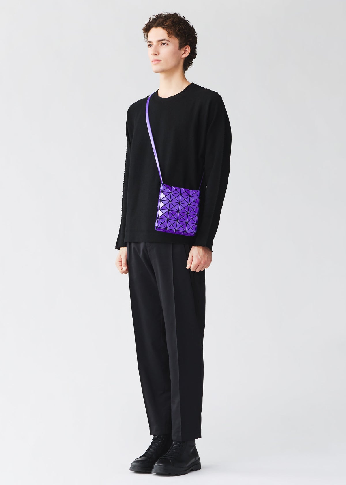 A person dressed in black holds a purple PRISM GLOSS crossbody bag from BAO BAO ISSEY MIYAKE, crafted from an enamel-like material, against a plain light background. view 10 of 10