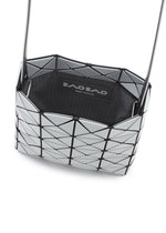 A close-up of a silver geometric-patterned BAO BAO ISSEY MIYAKE PRISM GLOSS shoulder bag, crafted from an enamel-like material with black accents and a visible brand label inside.