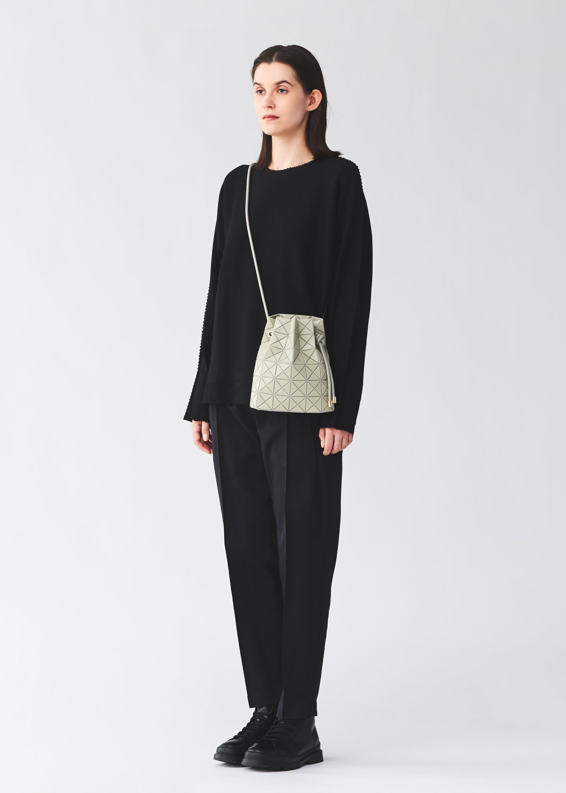 Zoomed view A person stands against a plain background, dressed in a loose black sweater, black pants, and black shoes, carrying the BAO BAO ISSEY MIYAKE WRING CLAY—a small nubuck-like geometric-patterned shoulder bag.
