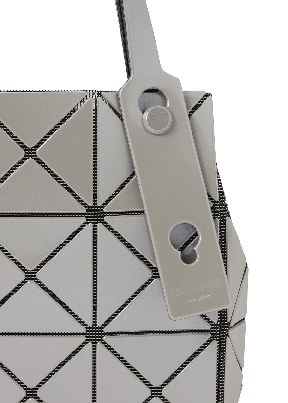 Close-up of the CARAT handbag by BAO BAO ISSEY MIYAKE, showcasing its geometric design with gray triangular panels and black seams, crafted from a sleek metallic material. A matching gray tag with circular cutouts and embossed text is attached to the handle. view 7 of 9