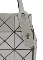 Close-up of the CARAT handbag by BAO BAO ISSEY MIYAKE, showcasing its geometric design with gray triangular panels and black seams, crafted from a sleek metallic material. A matching gray tag with circular cutouts and embossed text is attached to the handle.