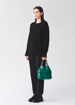 A person dressed in black holds the BAO BAO ISSEY MIYAKE CARAT handbag, featuring a green geometric metallic design and a zippered pocket, against a plain, light-colored background.