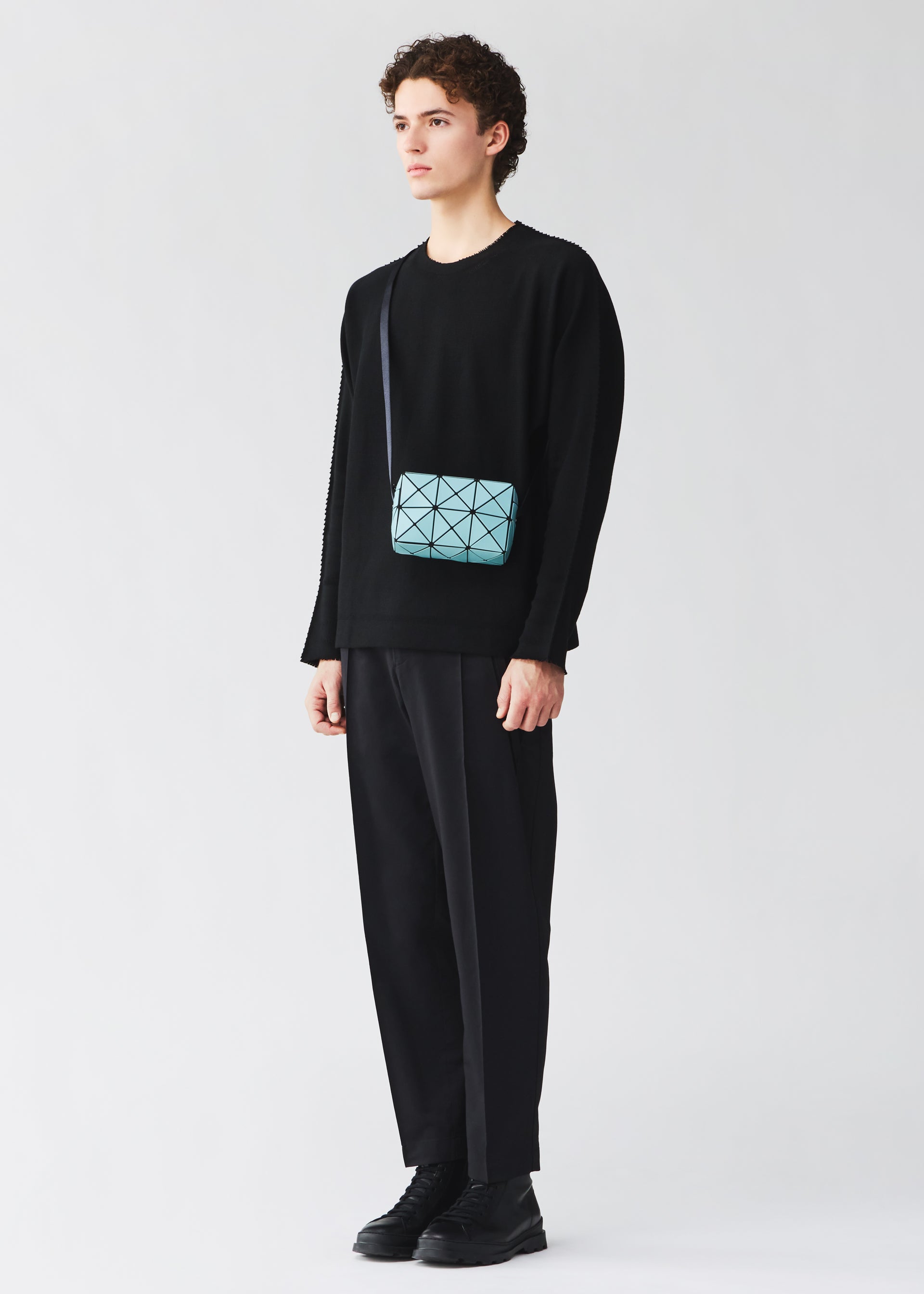 Zoomed view Against a plain background, a person wears a black sweater, black pants, and black shoes. They complete the look with the BAO BAO ISSEY MIYAKE CUBOID bag—a small, light blue minimalist piece featuring an adjustable strap worn crossbody.