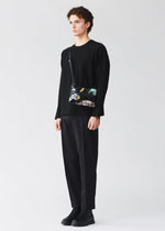 A person stands against a plain background, wearing a black sweater, black pants, black shoes, and carrying the BAO BAO ISSEY MIYAKE COSMIC shoulder bag, which features a geometric design with colorful accents and an adjustable strap for added comfort and versatility.