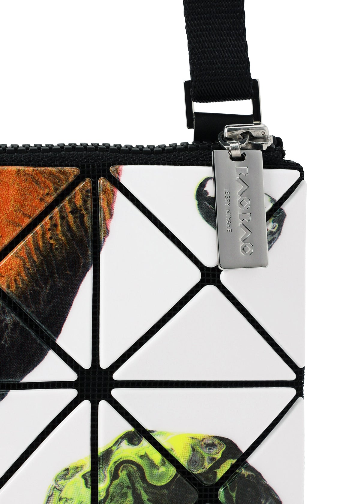 Close-up of the BAO BAO ISSEY MIYAKE COSMIC shoulder bag, featuring geometric white enamel triangular panels with abstract colorful accents and a prominent black adjustable strap. A silver tag attached to the zipper displays the brand name. view 7 of 10