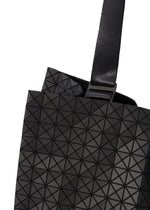 Close-up of a CART tote bag by BAO BAO ISSEY MIYAKE, featuring a black geometric-patterned design with adjustable handles and a wide textured strap. Raised triangles form a striking grid, making it ideal as an A4 laptop bag.
