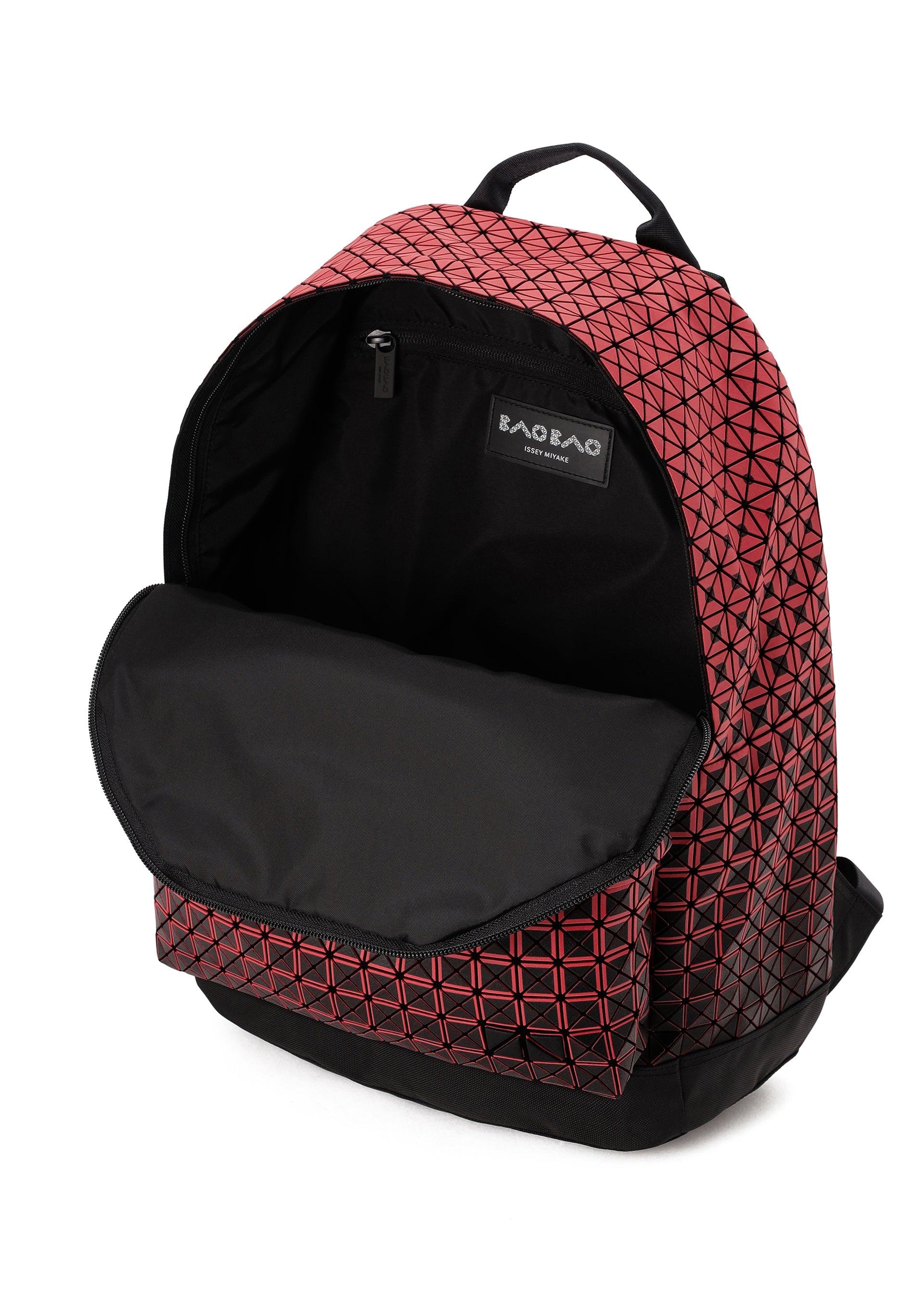 Zoomed view A red geometric-patterned DAYPACK GRADUAL backpack from BAO BAO ISSEY MIYAKE, distinguished by its striking three-dimensional shape, features a black inner lining and a front flap that opens to reveal the spacious main compartment and a small inner pocket adorned with a visible BAOBAG label.