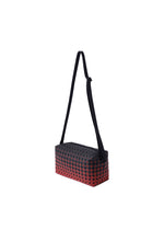 SADDLE BAG GRADUAL by BAO BAO ISSEY MIYAKE is a rectangular crossbody bag from the KURO series, showcasing a bold geometric black grid pattern over a striking red graphic gradation background with a long adjustable black strap. This box-shaped shoulder bag is photographed on a plain white background.