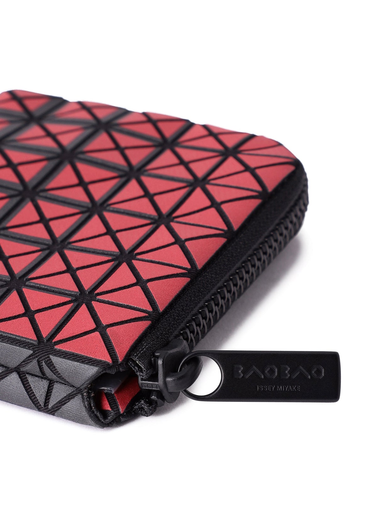 Close-up of the CLAM WALLET GRADUAL by BAO BAO ISSEY MIYAKE, a red zippered pouch featuring black geometric triangle patterns and a black zipper pull with the brand’s logo—perfect for use as a mini wallet or coin case, thanks to its practical L-shaped zipper that allows easy access. view 7 of 8
