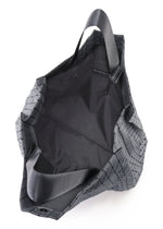 The CART REFLECTOR by BAO BAO ISSEY MIYAKE is a black tote bag with a geometric pattern and adjustable handles, shown from above to display its spacious, unlined interior and a small inner label.