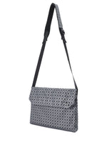 The FROGGY REFLECTOR by BAO BAO ISSEY MIYAKE is a grey and black shoulder bag with a modern geometric triangle pattern, cushioned adjustable long strap, flap closure, and roomy storage for daily essentials.