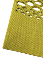 A close-up of the MOKKO BASKET by GOOD GOODS ISSEY MIYAKE shows its yellow textured surface with diagonal lines and oval cutouts in the upper right corner.