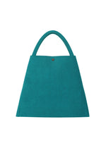 The KURURI by GOOD GOODS ISSEY MIYAKE is a teal, trapezoid-shaped handbag featuring a sturdy handle and small button closure at the top center, displayed against a white background.