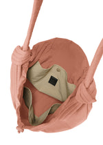 A top view of the pink FUWA FUWA fabric shoulder bag by GOOD GOODS ISSEY MIYAKE, featuring knotted straps inspired by Japanese zero-waste design. The beige-lined interior includes a buttoned pocket and a small black label.