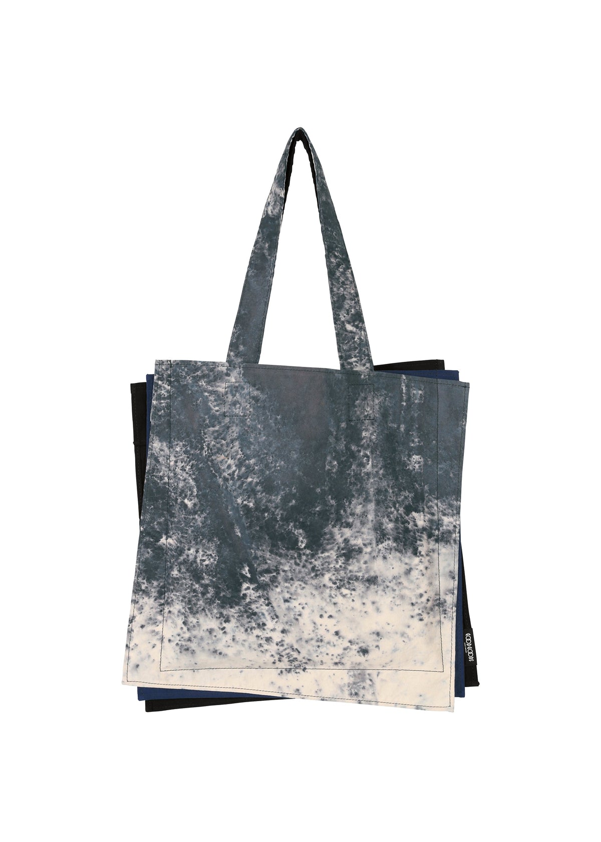 The IROGAMI SALT DYE tote from GOOD GOODS ISSEY MIYAKE features long handles and a blue-and-white marbled tie-dye inspired by Shio-zome. As part of the IROGAMI series, it's layered over a dark solid bag in the background. view 1 of 10