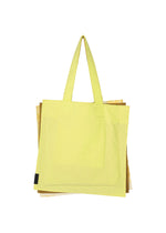 A large yellow IROGAMI SALT DYE tote bag by GOOD GOODS ISSEY MIYAKE, featuring Shio-zome dyeing and two shoulder straps, is shown on a plain white background with part of a brown or gold bag partially visible behind it.