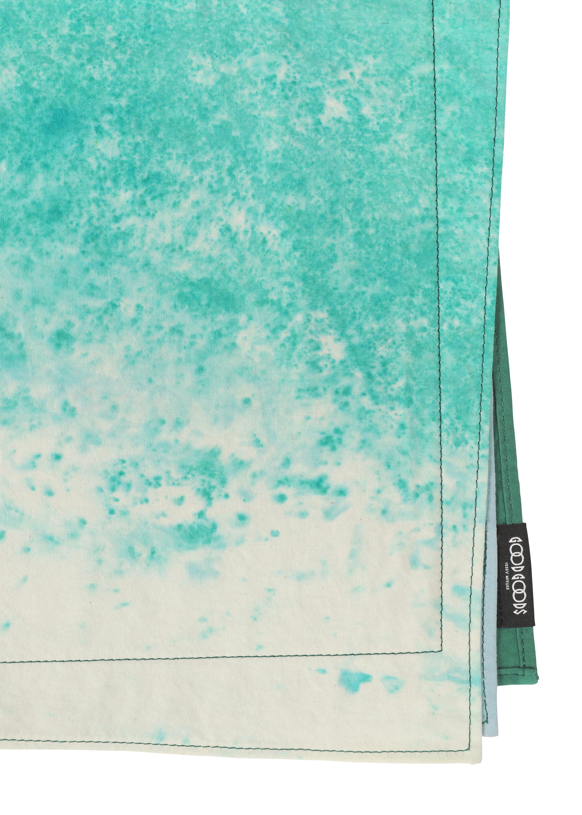Zoomed view A close-up of aqua and white tie-dye cloth napkins from the IROGAMI SALT DYE collection by GOOD GOODS ISSEY MIYAKE, featuring neat stitching, a black “ECOVISION” label, Shio-zome dyeing, and a soft, textured look.