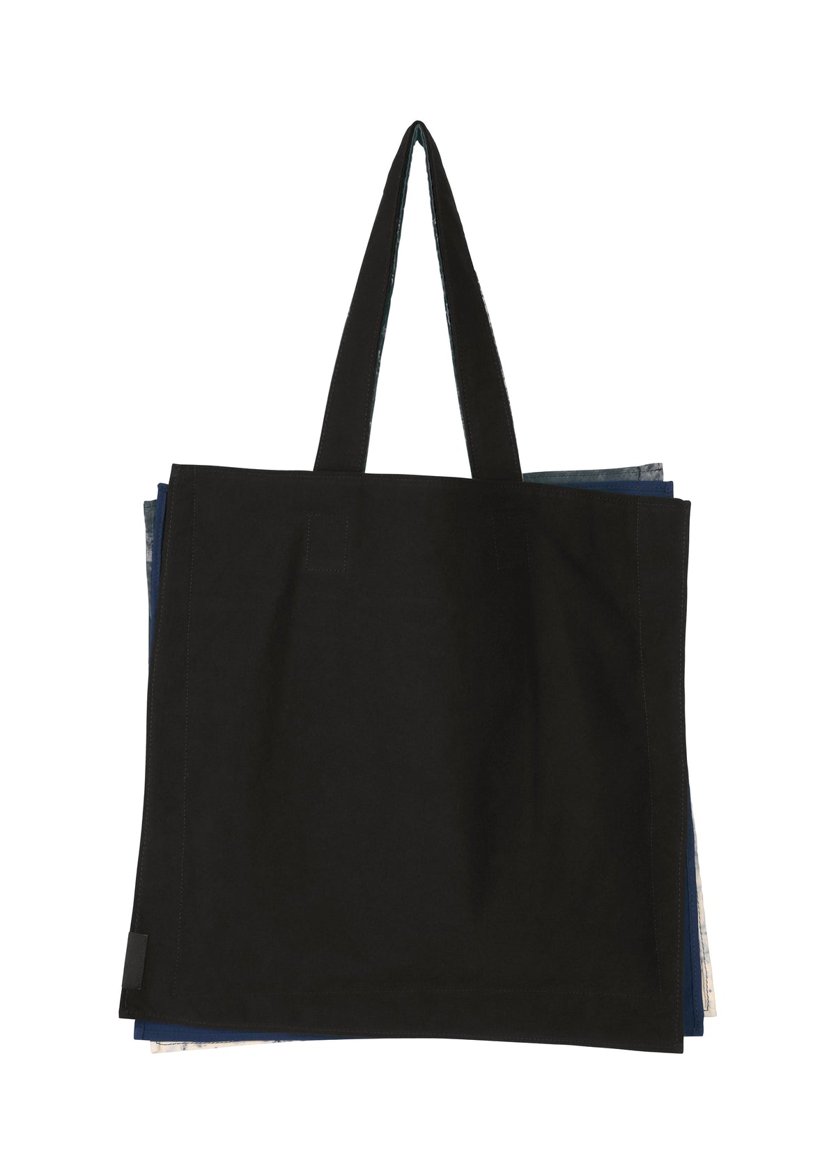 A large black IROGAMI SALT DYE tote bag by GOOD GOODS ISSEY MIYAKE with two handles, photographed on a white background. Edges of layered, salt-dyed patterned fabric peek out from behind the main bag. view 2 of 10