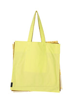 A large, light yellow IROGAMI SALT DYE tote bag by GOOD GOODS ISSEY MIYAKE with two handles. Part of a gold or beige object peeks out from behind. Set against a plain white background. Features unique Shio-zome dyeing technique.