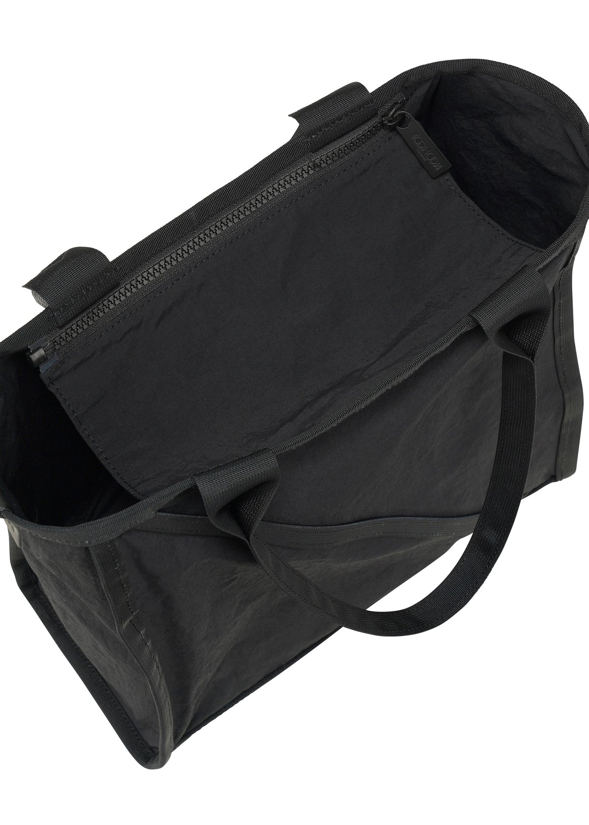 The WAKU tote bag by GOOD GOODS ISSEY MIYAKE is black with short handles, wide gussets, an open top, and an internal zippered pocket. Its interior and texture are visible from an angled above view. view 3 of 6