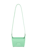 The BOX by GOOD GOODS ISSEY MIYAKE is a minimalist pastel green convertible shoulder bag featuring a long strap and simple flap closure, shown against a white background.
