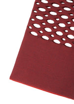 A close-up of the MOKKO BASKET by GOOD GOODS ISSEY MIYAKE highlights its red textured surface with large, oval diagonal cutouts revealing a white background.