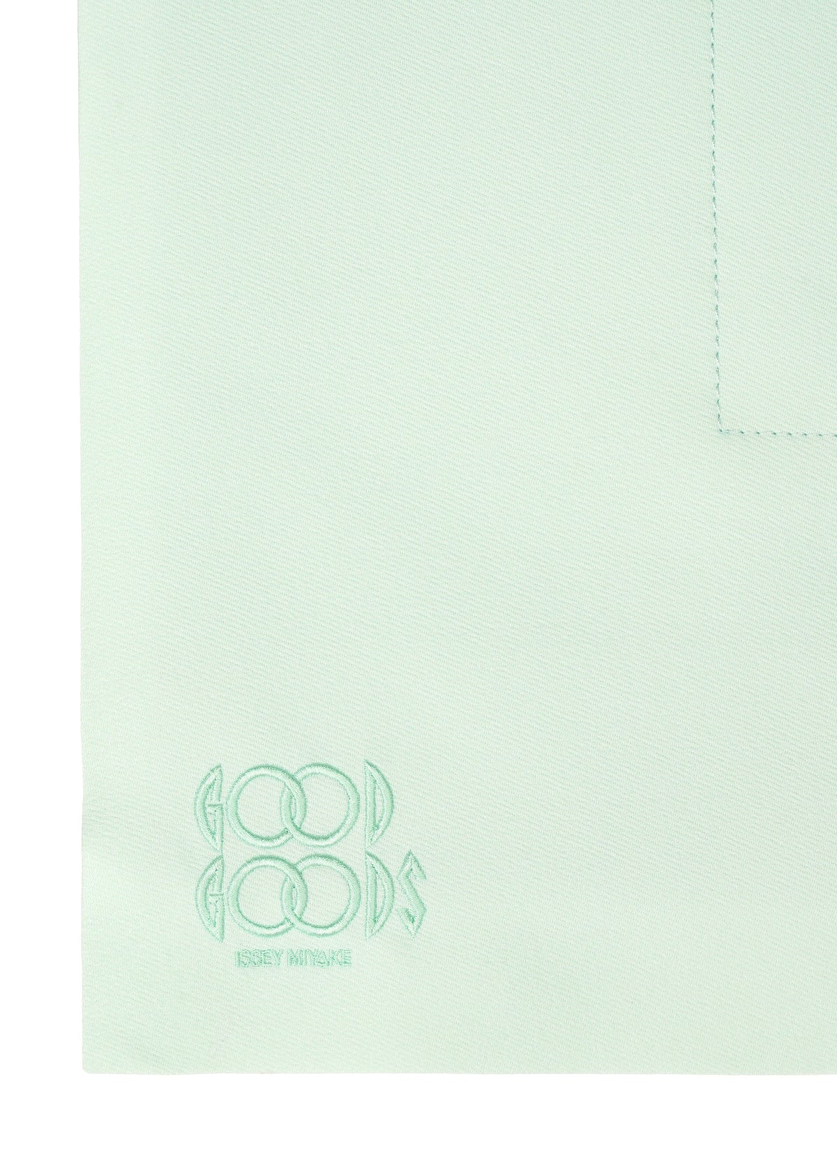 A close-up of ROLL by GOOD GOODS ISSEY MIYAKE shows light mint green fabric with an elegant sheen, visible seam, and embroidered logo text in one corner. view 5 of 7