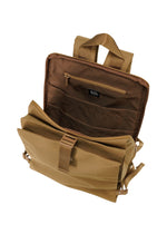 The JABARA backpack by GOOD GOODS ISSEY MIYAKE in tan is shown with its top flap open, revealing an interior zippered pocket, organizer slots, a laptop sleeve, two handles, and adjustable shoulder straps against a white background.