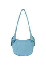 The FUWA FUWA by GOOD GOODS ISSEY MIYAKE is a light blue fabric shoulder bag with a rounded silhouette, featuring a long strap and distinctive knot accents at each side where the strap meets the bag—an effortless design inspired by traditional Japanese noragi style.