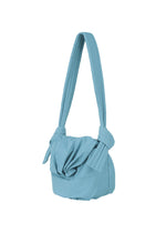 The FUWA FUWA by GOOD GOODS ISSEY MIYAKE is a light blue fabric shoulder bag featuring a wide, padded strap knotted at both ends where it connects to the soft, unstructured body. The front of the bag showcases a gathered, knotted detail—a subtle nod to Japanese noragi and its emphasis on relaxed, artisanal craftsmanship.