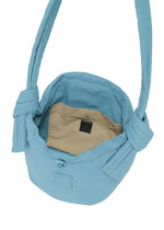Introducing the FUWA FUWA shoulder bag by GOOD GOODS ISSEY MIYAKE: a light blue, quilted fabric bag featuring wide straps with distinctive knot details, inspired by Japanese noragi aesthetics. The open design reveals a beige inner pocket adorned with a dark label, while both interior and exterior colors are perfectly matched for a seamless effect. Thoughtfully crafted with zero-waste design principles.