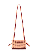 The MOKKO BI-COLOR crossbody knit bag by GOOD GOODS ISSEY MIYAKE features a rectangular shape, long strap, peach and burgundy colors, perforated front pattern, and a washable design for easy care.