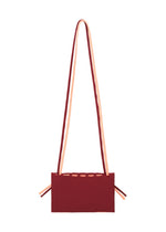 The MOKKO BI-COLOR by GOOD GOODS ISSEY MIYAKE is a rectangular burgundy knit tote with peach straps and side ties, shown on a white background. Stylish, practical, and washable.