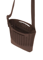 The MOKKO MONO GRIP by GOOD GOODS ISSEY MIYAKE is a brown crossbody bag featuring a woven, basket-like texture with horizontal slits for a modern, airy look. It has an open top and an adjustable shoulder strap, making this tote both stylish and functional.