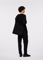 A person with curly hair, dressed in all black, stands facing away, holding a large black business bag with an adjustable shoulder strap over their shoulder against a plain white background.