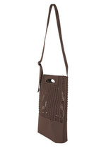 The MOKKO MONO GRIP by GOOD GOODS ISSEY MIYAKE is a brown shoulder bag accented with a laser-cut perforated pattern on the front. It features an adjustable shoulder strap and a built-in handle hole near the top. With its modern, minimalist design, this bag is perfect both as a sleek business accessory and as a versatile tote for everyday use.