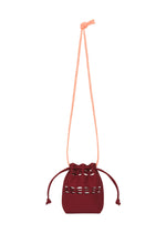 The MOKKO POCKET BI-COLOR by GOOD GOODS ISSEY MIYAKE is a small maroon drawstring bag with a long light pink strap and decorative cutout details, shown on a white background. - BORDEAUX （no.84）