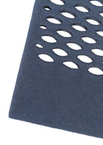 Close-up of MOKKO WASHI by GOOD GOODS ISSEY MIYAKE, showing a dark blue textured surface with oval cut-out holes in rows, evoking a washi paper tote bag, set diagonally on a white background.