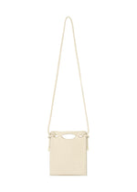 The MOKKO WALE by GOOD GOODS ISSEY MIYAKE is a small beige rectangular shoulder bag with vertical stripes, a cut-out handle, long strap, and side knots.