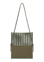 The MOKKO WALE by GOOD GOODS ISSEY MIYAKE is a square woven shoulder bag in olive green with an open-weave top, solid bottom, long strap, side knots, and subtle striped details.